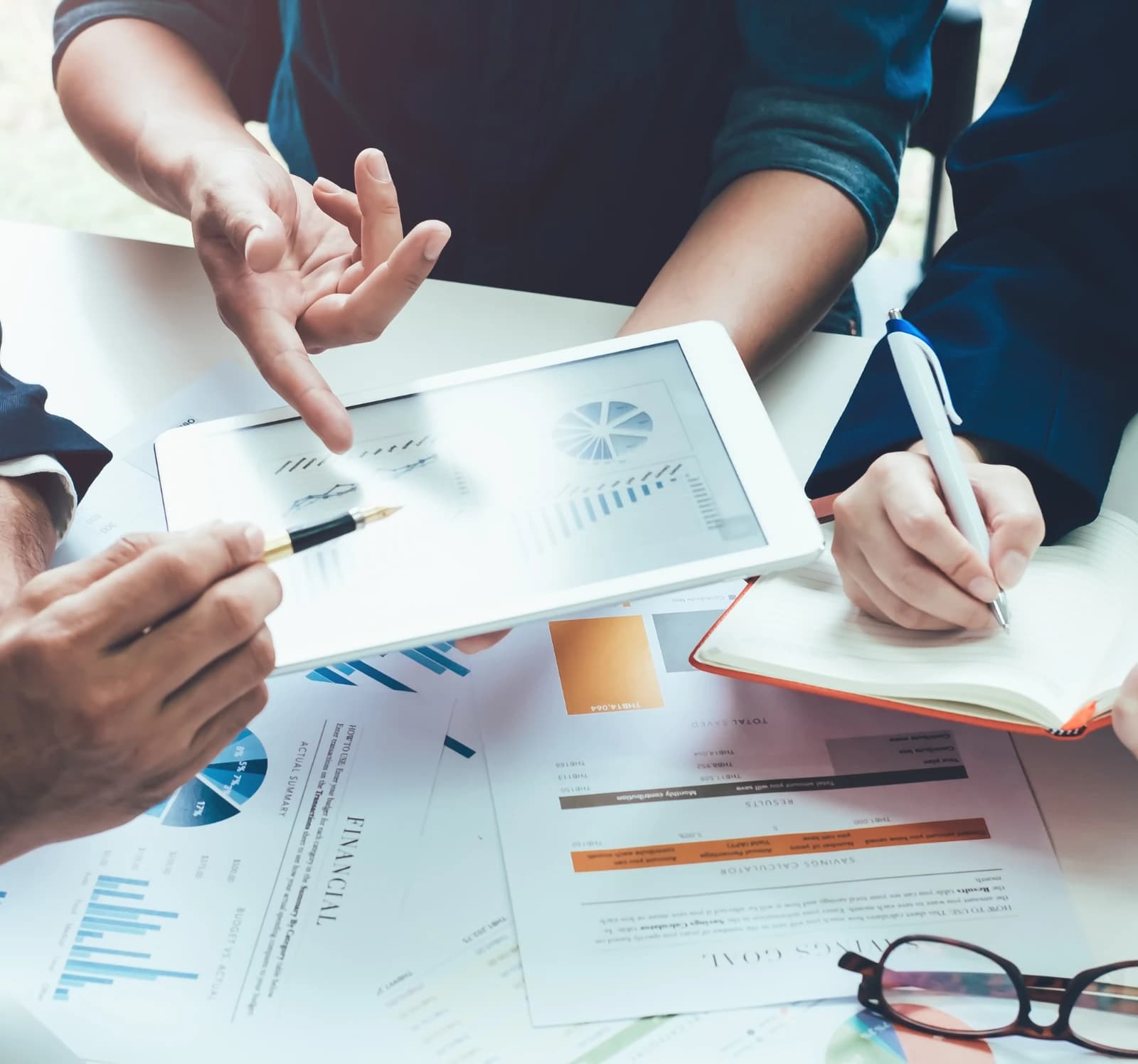 Three people going over financial charts on a tablet and printouts
